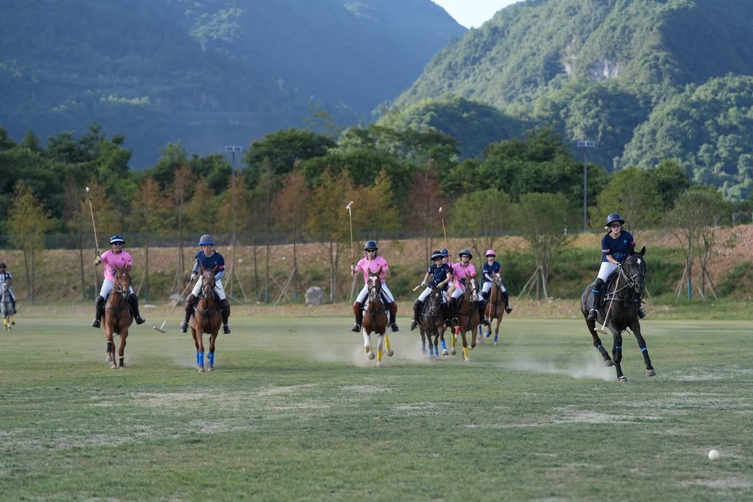 A polo match in play on the grass field at 1003 Polo Club, with the mountains of Wulong behind