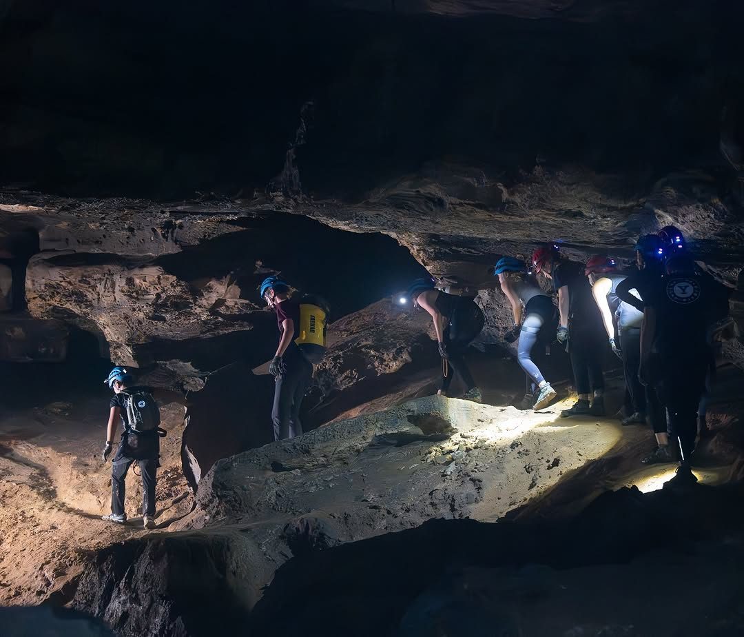 A group exploring a vast cave with headlamps