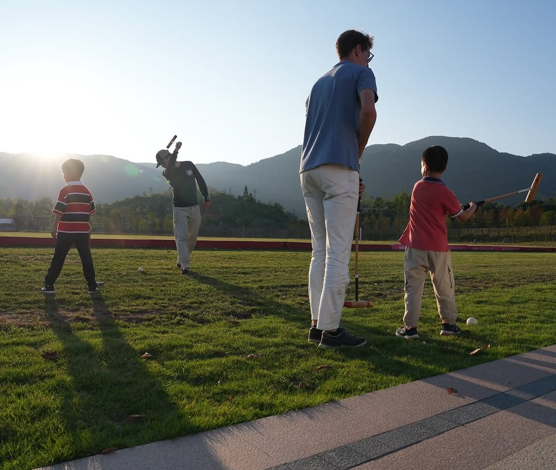 A player and two young children practising stick-and-ball at sunset